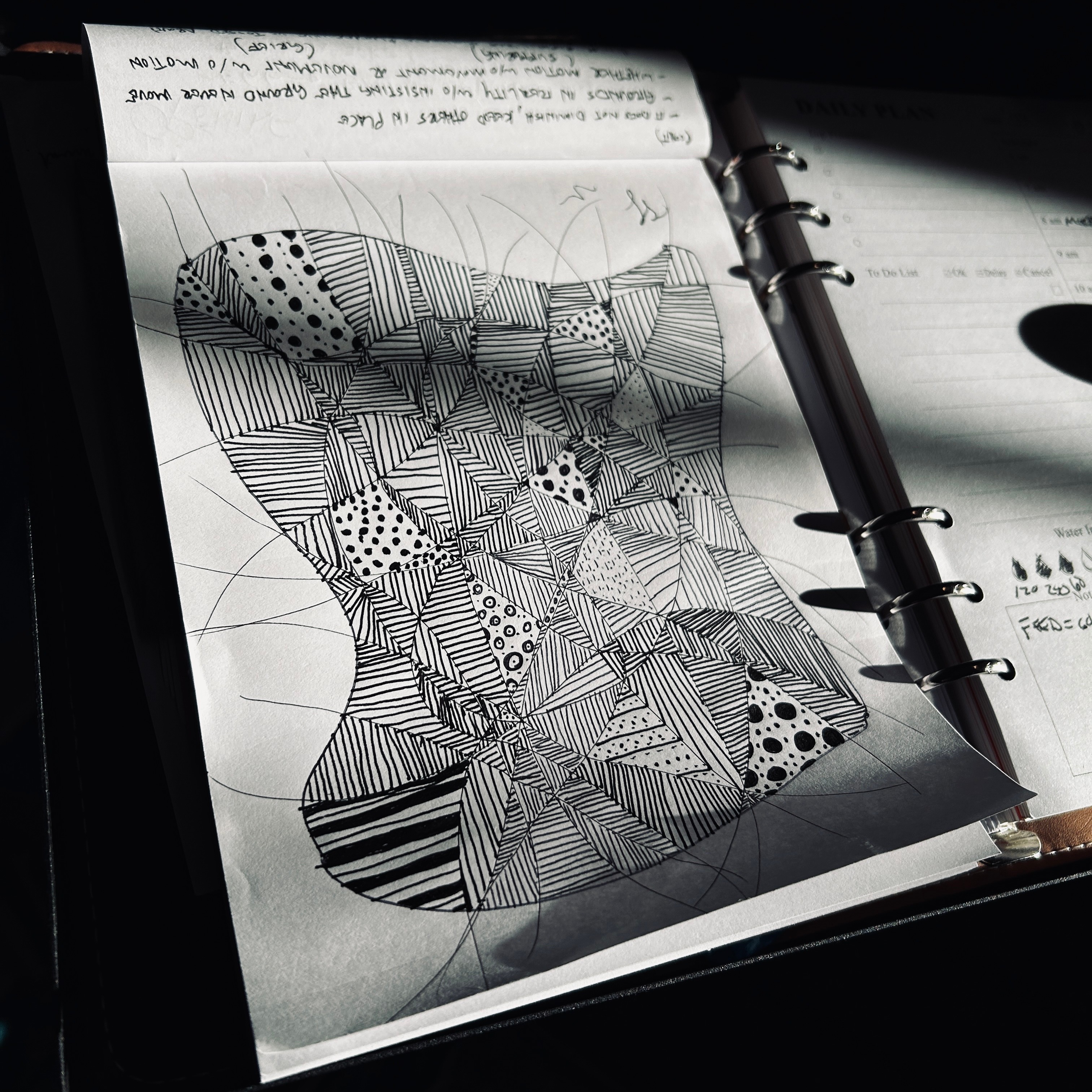 A black and white line drawing in a sketchbook showing geometric blocks with various patterns (lines, dots, crosshatching) creating a 3D optical illusion that appears to rise from the page.